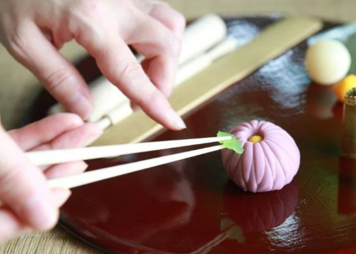 Someone is using chopsticks to add a leaf detail to a pink wagashi in this Enoshima wagashi-making class.